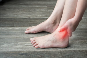 Close-up of woman hands holding and touching her ankle, suffering from ankle pain. Ankle pain may be caused by an injury, like a sprain, or by a medical condition, such as arthritis.
