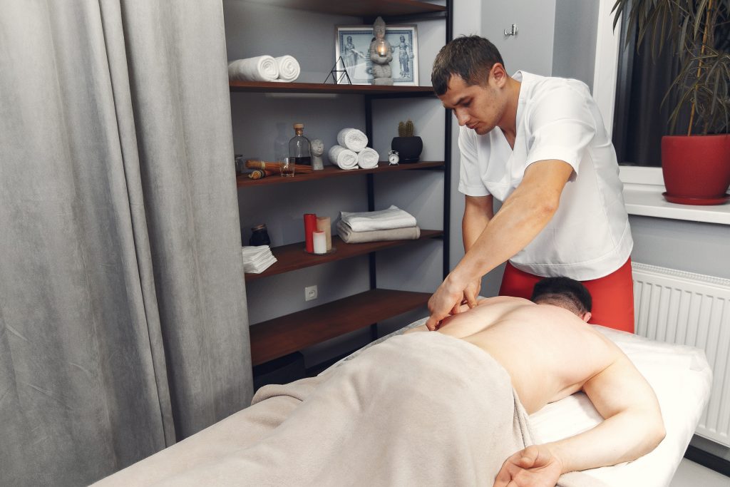 sports massage therapist performing physio treatment on the left shoulder blade of man lying face down in a physiotherapy clinic
