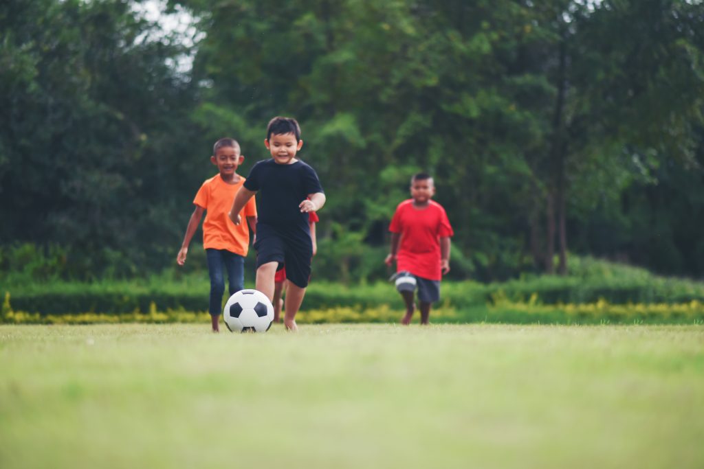 young children playing with a football in green field